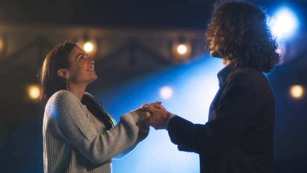 Man and woman theater actors holding hands during a rehearsal of a romantic play on a stage illuminated by a spotlight