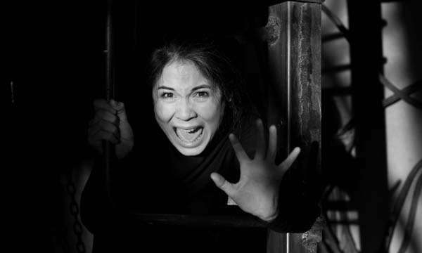 A black and white portrait of the emotional and screaming from fear of a woman with dark hair, looking frightenedly not light putting her hand in front of her in the dark room of an abandoned building
