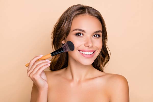 Photo of young happy smiling beautiful woman doing contouring apply blush on cheeks isolated on beige color background